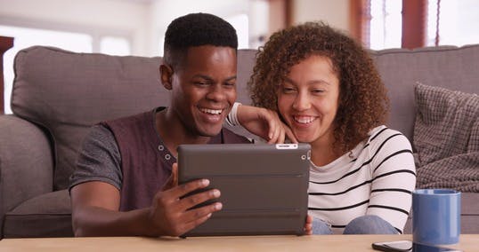 A man and a women laughing while staring at their iPad